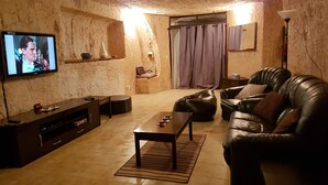 Un salon comprenant un canapé en cuir, une table basse, un téléviseur fixé au mur et une petite étagère ornée d’objets décoratifs.