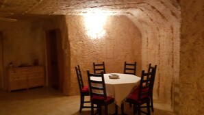 Un coin repas comprenant une table ronde et quatre chaises, un buffet en bois et un mur en pierre à la texture particulière.