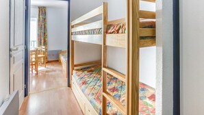 A room with bunk beds, a wooden floor, a chair, and a door leading to another room. - Apartment Cauterets, 1 bedroom, 4 persons (Cauterets)