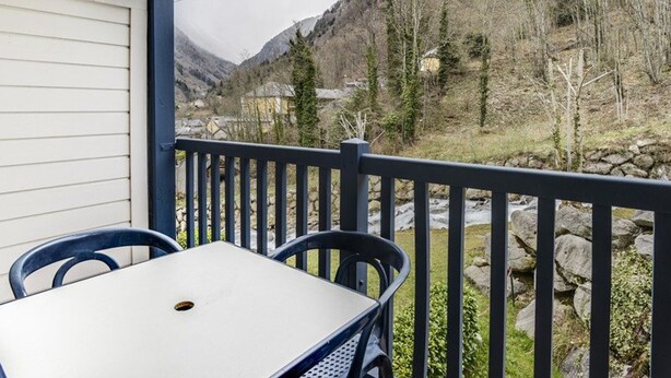 A balcony with a table and chairs, overlooking a mountainous landscape with a view of houses and a stream. - Apartment Cauterets, 1 bedroom, 4 persons (Cauterets)
