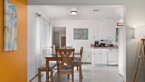 Ein Essbereich mit Holztisch und -stühlen, eine Küche mit weißen Schränken und ein Bild an der Wand.