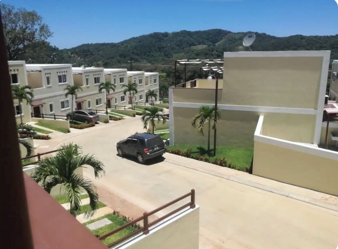 A residential area with modern buildings, a car parked on the street, and a mountain in the background.