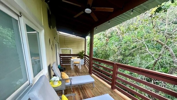 Eine Holzterrasse mit zwei Liegestühlen und einem Tisch, mit Blick auf eine üppige grüne Landschaft.