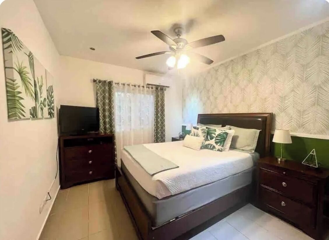 A bedroom with a bed, a ceiling fan, a TV, and a dresser.