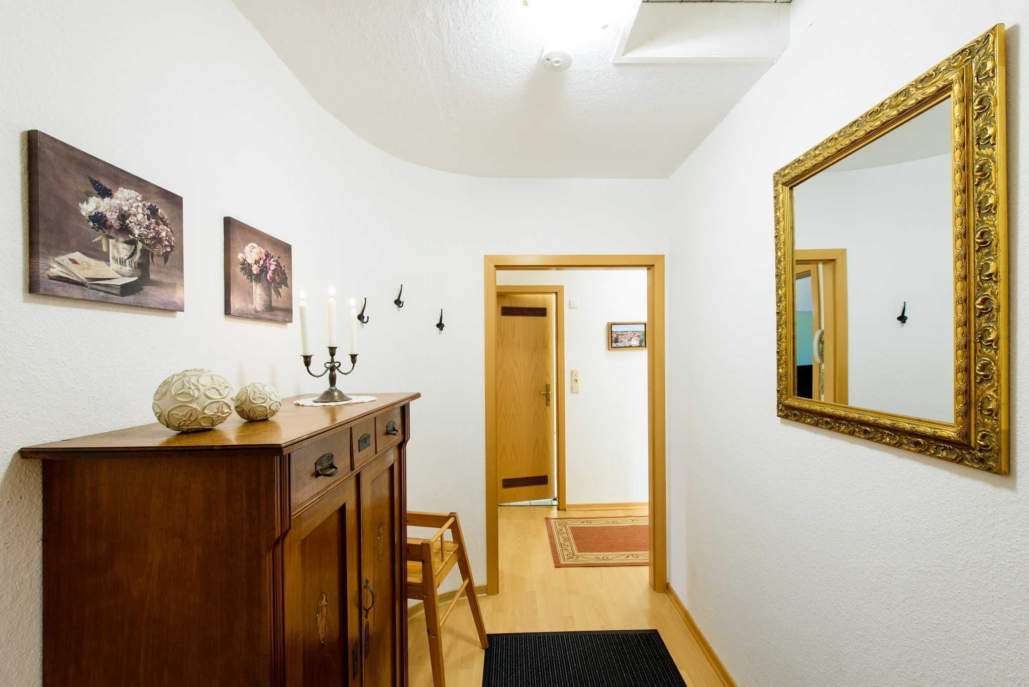 A hallway with a wooden dresser, two paintings, a candelabra, and a large ornate mirror.