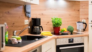 Eine moderne Küche mit Holzausstattung, einer schwarzen Kaffeemaschine, einem roten Topf mit Basilikum, einer Obstschale und einem kleinen Topf mit Pflanze.