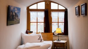 Ein Schlafzimmer mit Bett, Nachttisch, Lampe, einem Fenster mit Vorhängen, einem gerahmten Bild an der Wand und einem Fahrrad vor dem Fenster.