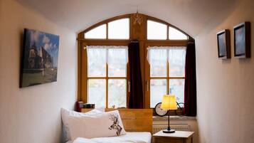 Ein Schlafzimmer mit Bett, Nachttisch, Lampe, einem Fenster mit Vorhängen, einem gerahmten Bild an der Wand und einem Fahrrad vor dem Fenster.