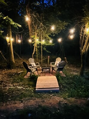 An outdoor seating area with a round table and four chairs, surrounded by trees and string lights.