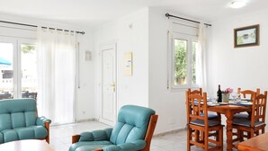 A dining area with a wooden table and chairs, a teal armchair, and a view of the outdoors through a window.