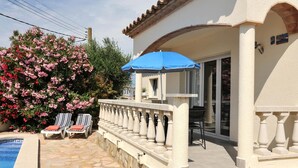 A poolside area with stone flooring, a blue umbrella, and two lounge chairs.