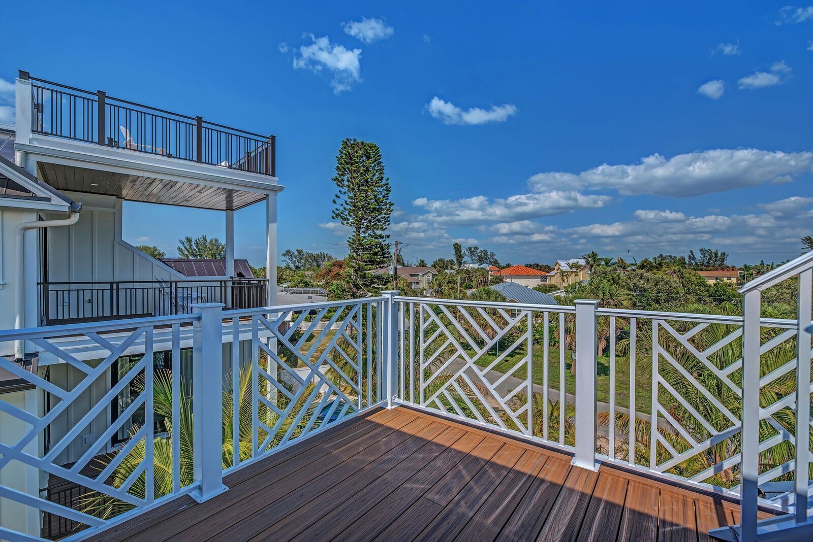 A wooden deck with white railings, a covered area with a balcony, and a view of a residential neighborhood.