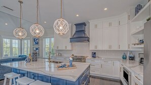 Una cocina moderna con muebles blancos, una isla grande con taburetes de bar, luces colgantes y un salpicadero de baldosas tipo espiga.