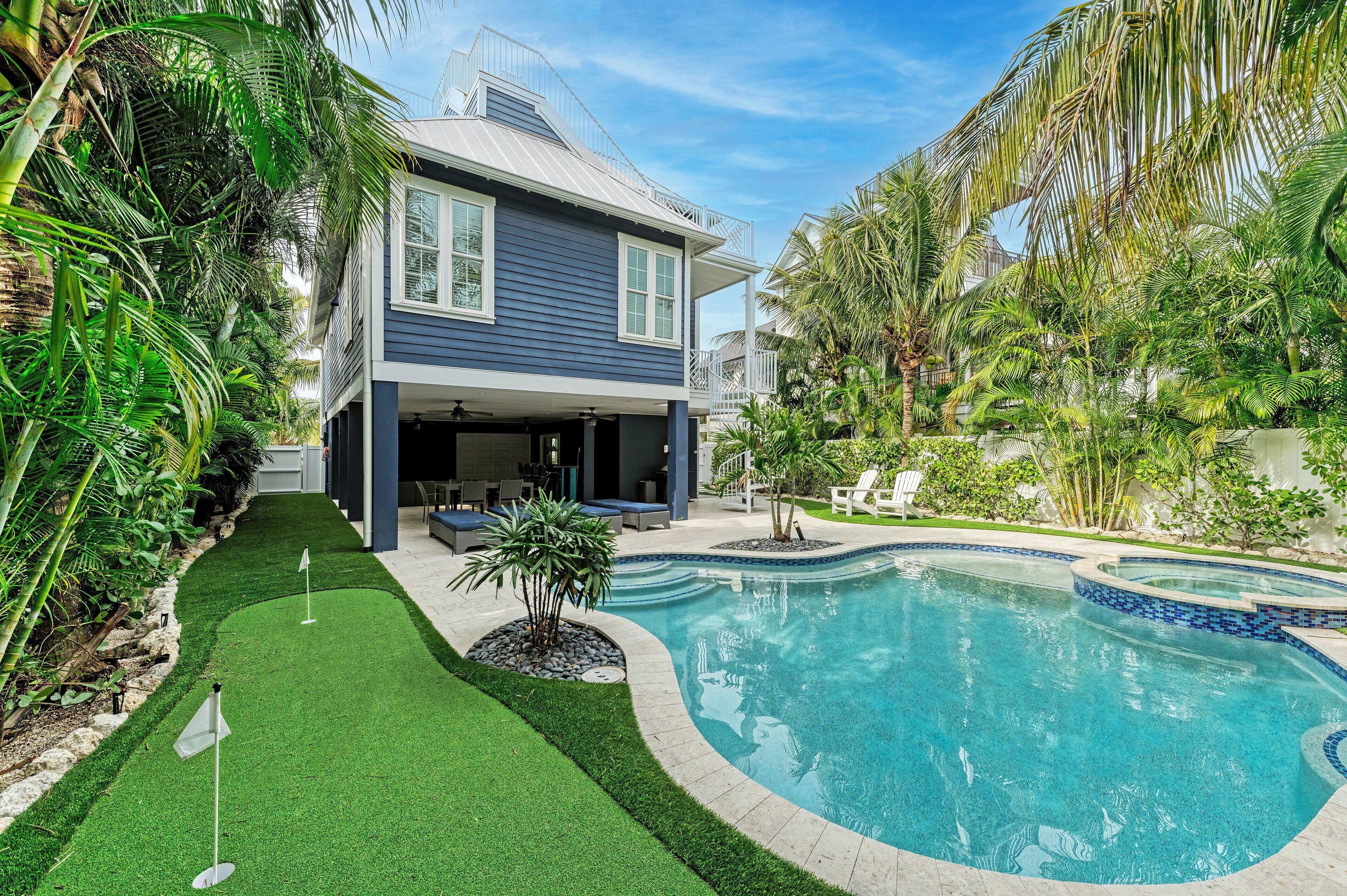 A two-story house with a swimming pool, surrounded by lush greenery and palm trees.