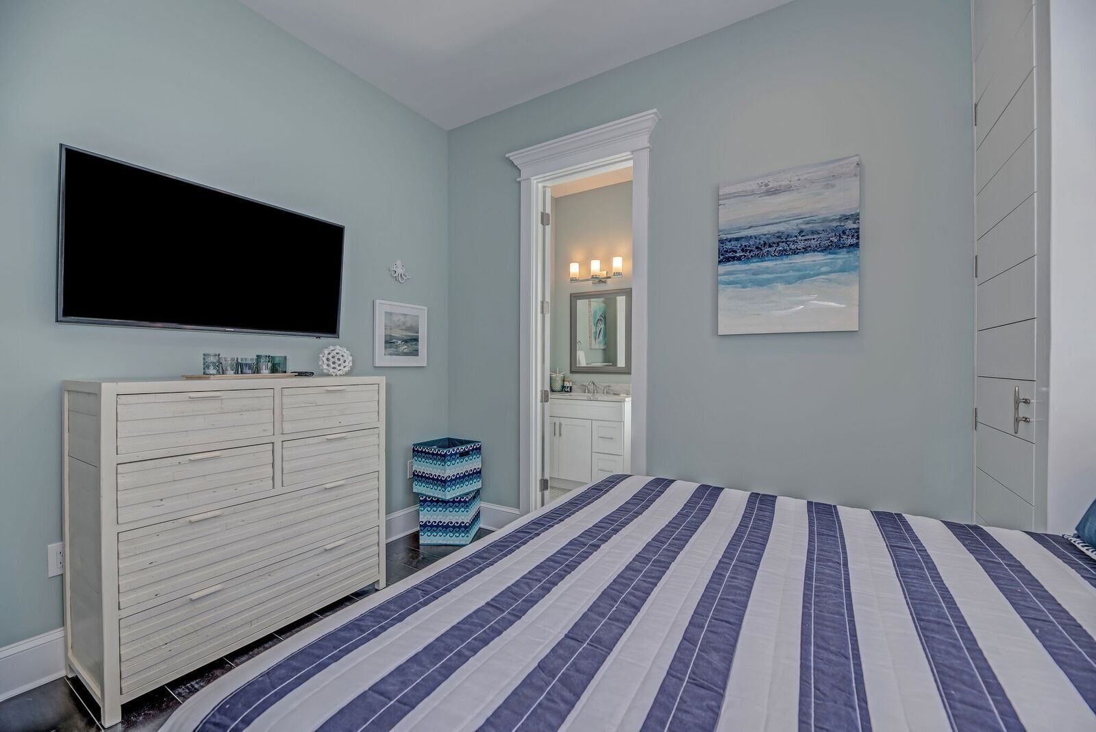 Un dormitorio con una cama grande, un aparador, un televisor, un baño con espejo y un cuadro en la pared.