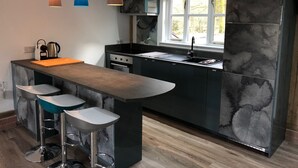 Ett modernt kök med en central köksö, barstolar, en diskho och hängande lampor.