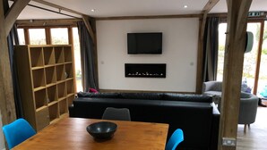 Ett mysigt rum med ett träbord, blå stolar, en svart soffa och en tv som är monterad på väggen.