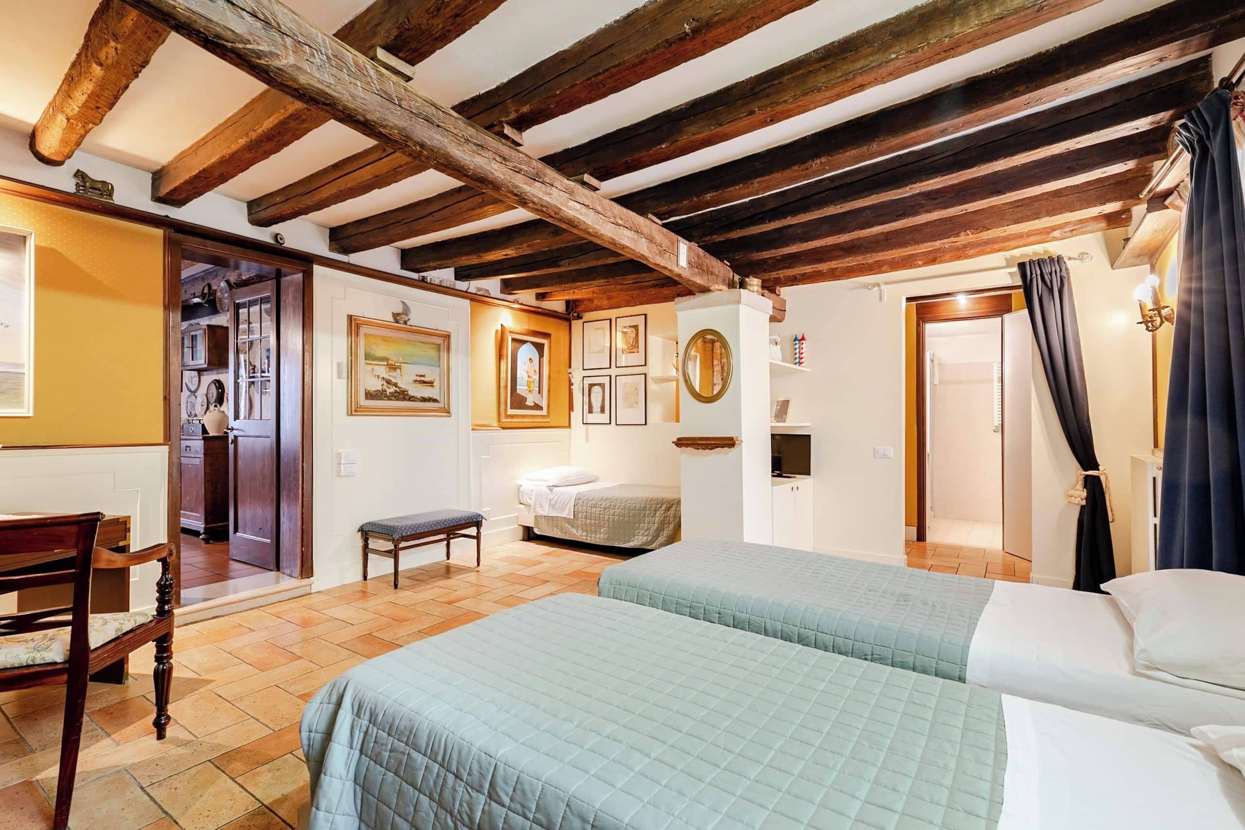 A bedroom with a bed, a bench, a chair, a door, and a wall with framed pictures.
