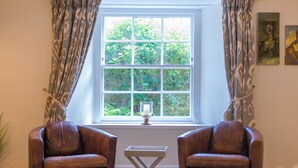 A room with two leather armchairs, a small table, and a window with a view of greenery.