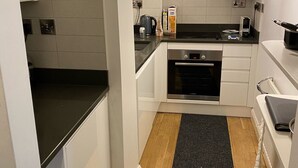 A compact kitchen with white cabinets, a black countertop, and a stainless steel range hood.
