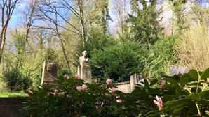 A statue in a garden with blooming flowers and trees in the background.