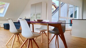 A modern dining area with a glass table, white chairs, and a wooden floor.