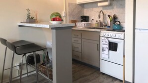 A compact kitchen with white cabinets, a built-in oven, a sink, and a small bar stool.