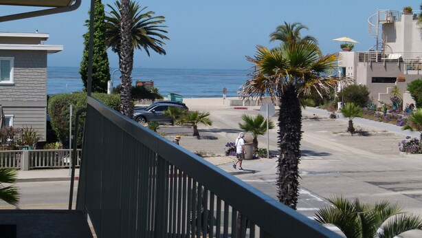 A coastal street with palm trees, a car, and a building with a spiral staircase.