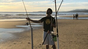 A person standing on a sandy beach holding fishing rods.