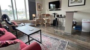 A modern living room with a sofa, chairs, a coffee table, a TV, and a small kitchen area.