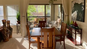Ein Essbereich mit Holztisch und -stühlen, einem Couchtisch mit Glasplatte und Blick ins Freie durch große Fenster.