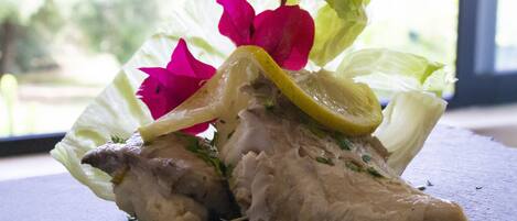 Un plato de comida con lechuga, una rodaja de limón y flores rosadas sobre una superficie oscura.