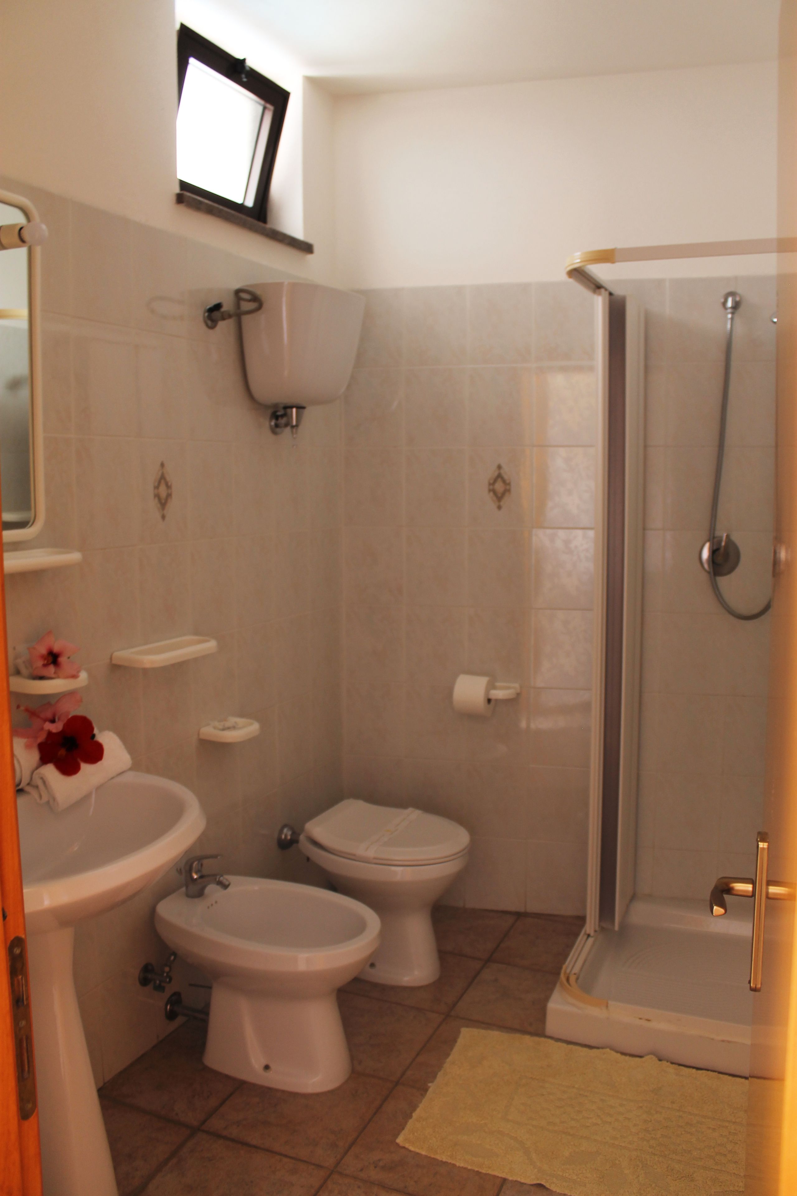 Un baño con inodoro, bidé, lavamanos y ducha con mampara de vidrio.