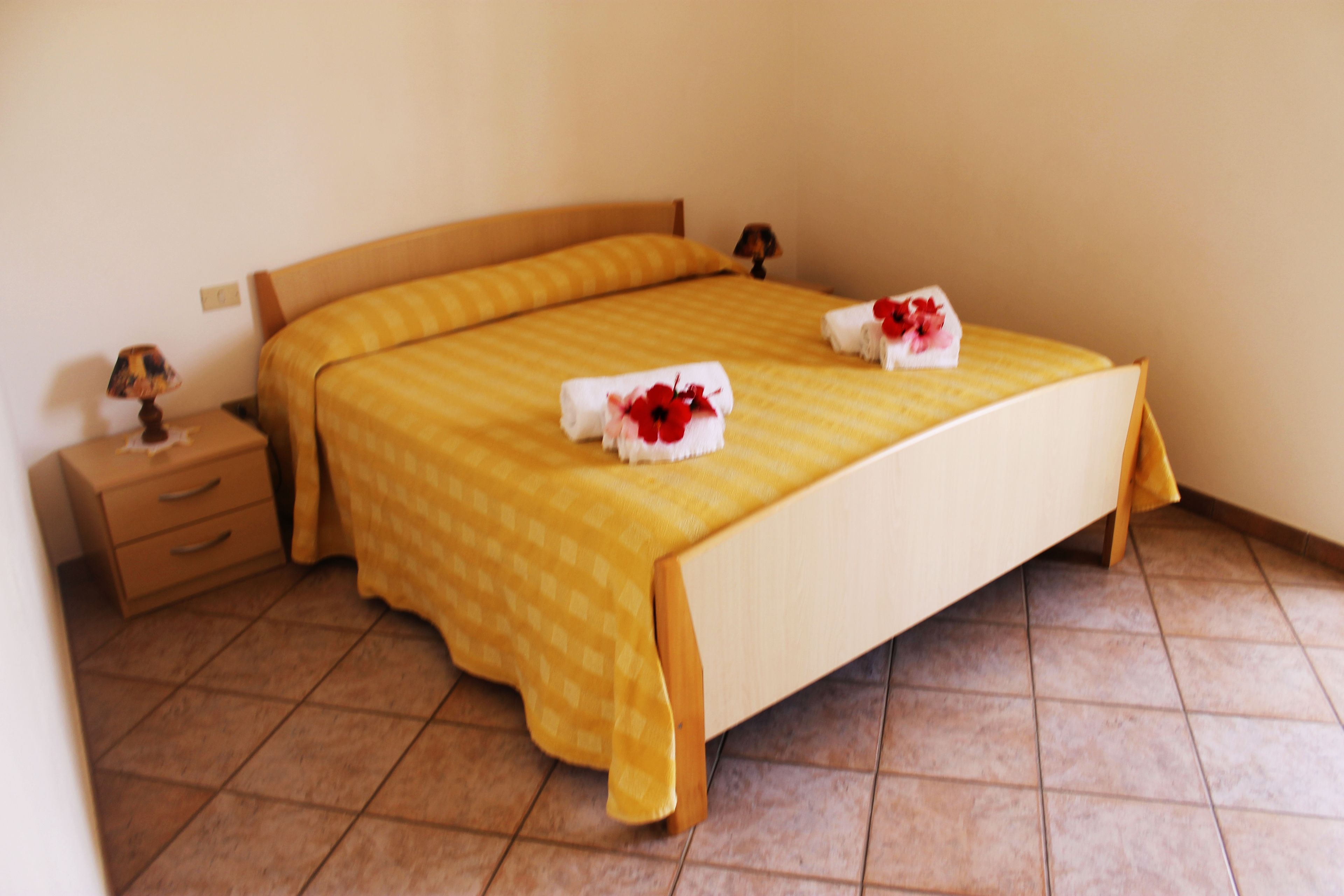 Ein ordentlich gemachtes Bett mit einer gelb karierten Bettdecke und zwei Handtüchern mit roten Blumenmotiven.
