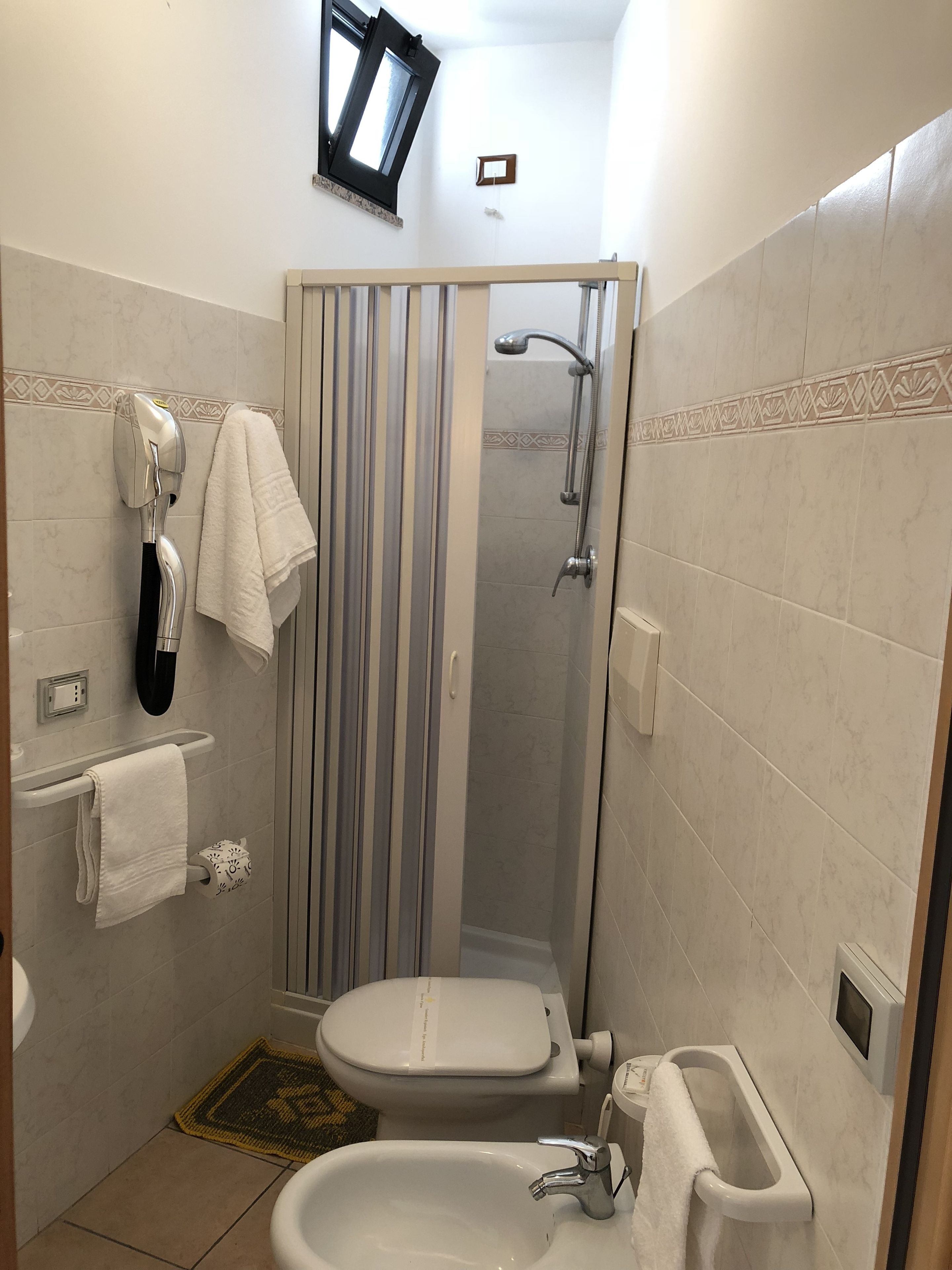A compact bathroom with a shower, toilet, sink, and towel rack.