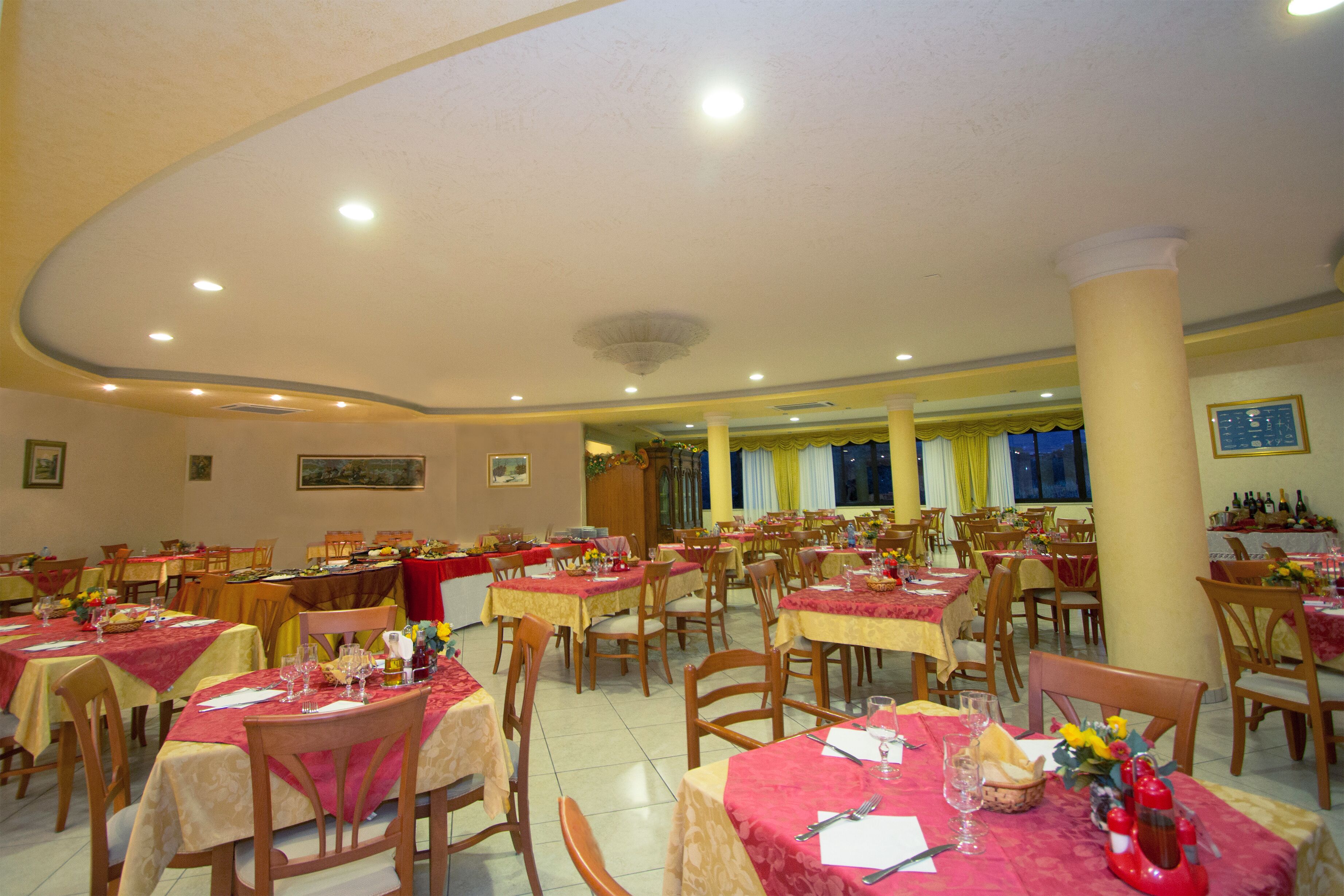 A dining area with multiple tables and chairs, arranged in a spacious layout with a high ceiling and recessed lighting.