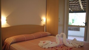 Una cama con una toalla dispuesta en forma de cisne y pétalos de rosa sobre un edredón estampado.