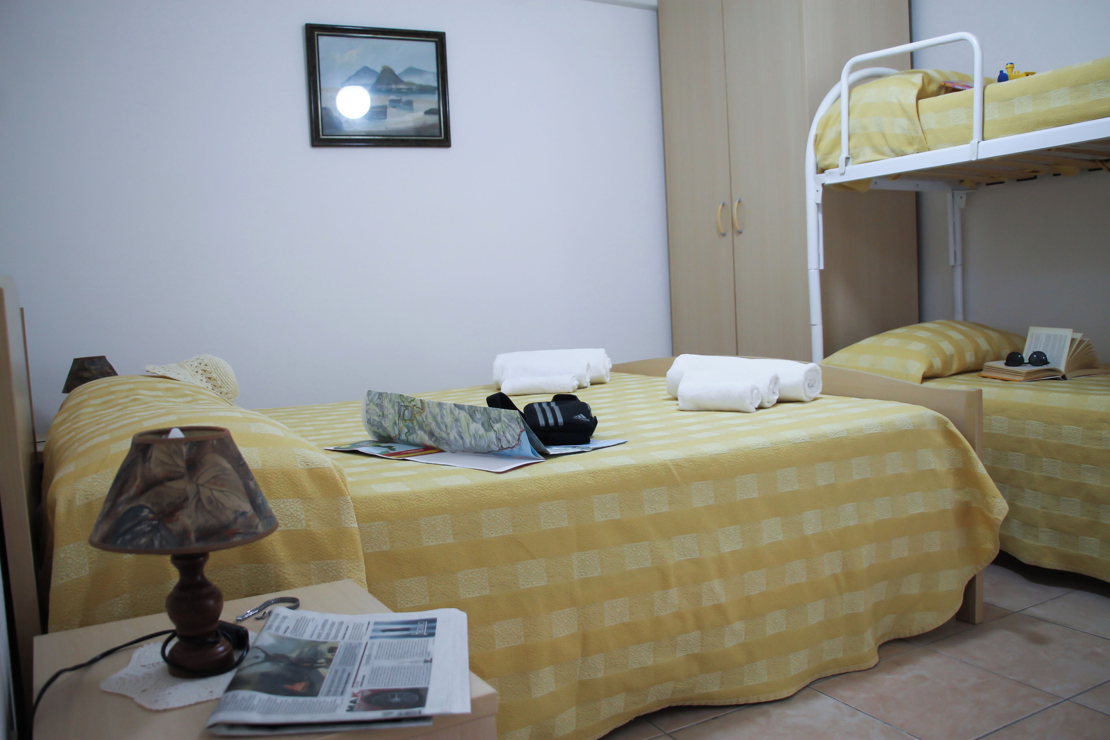 A hotel room with two beds, a lamp, a newspaper, and a framed picture on the wall.