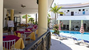Un patio de hotel con mobiliario exterior, una piscina y vistas al interior del edificio.