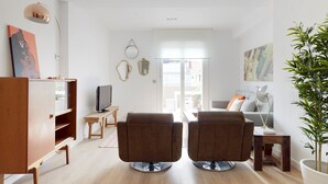 Un salon moderne avec deux fauteuils marron, un meuble en bois, un téléviseur et une plante en pot.