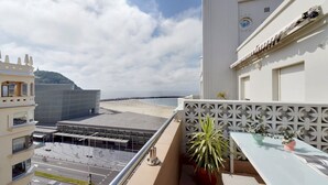 Un balcon donnant sur une plage, un parking et un immeuble à la façade blanche.