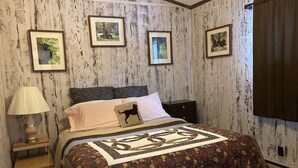 A bedroom with a bed, a nightstand, a lamp, and framed pictures on the wall. - Comfortable 3 Bedroom Cabin On the Shores of Lake Chippewa Flowage in Hayward WI (Hayward)