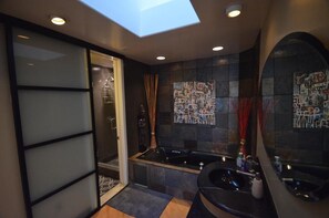 A modern bathroom with a skylight, a large bathtub, and a separate shower area. - California Tropical Resort Penthouse (Irvine)