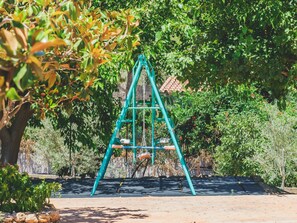 Children can play on the playground surrounded by lush greenery and trees.