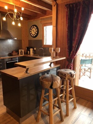 A cozy kitchen with wooden accents, a central island, stools, and a clock on the wall.