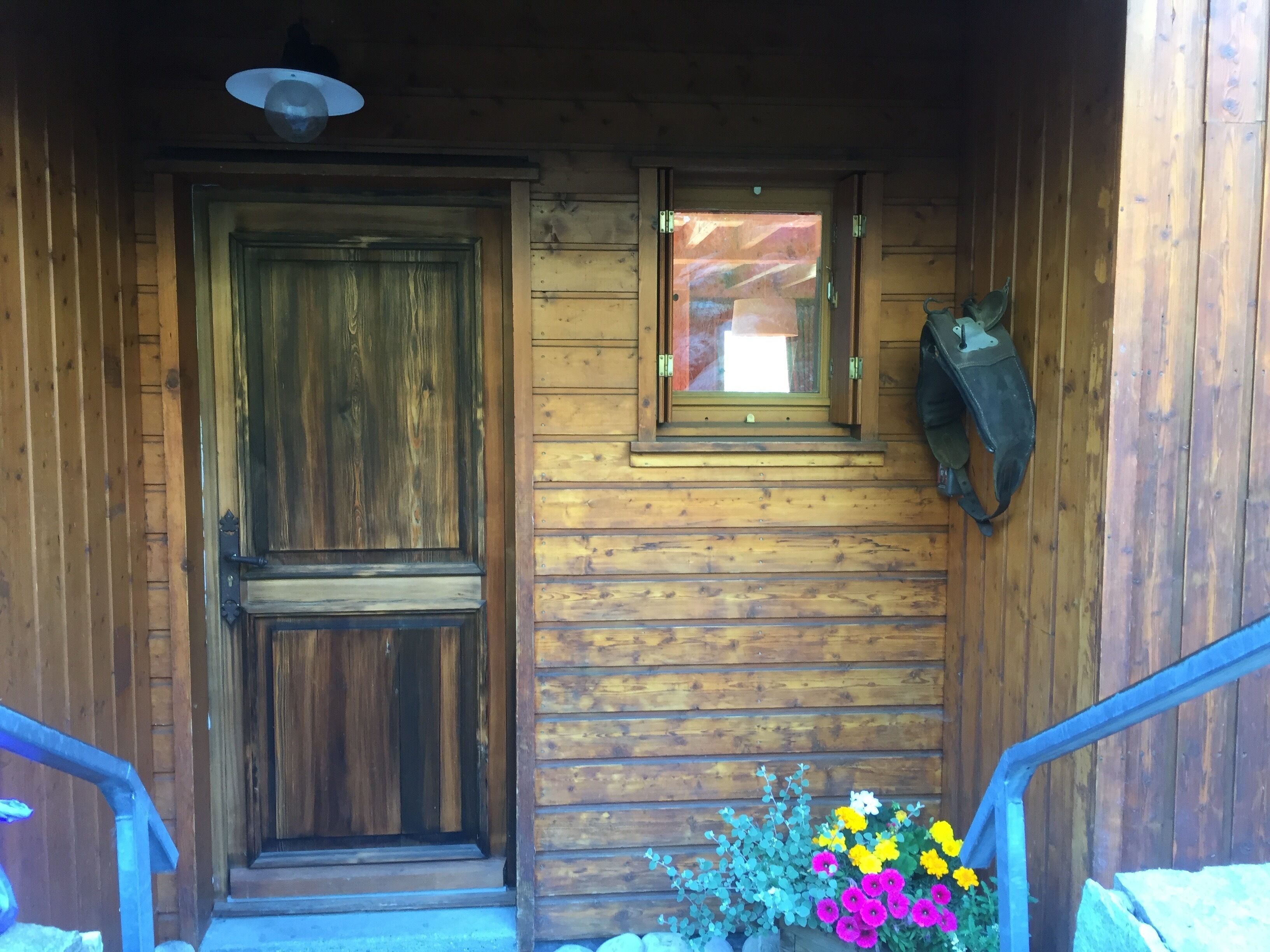 A wooden cabin entrance with a large door, a small window, and a flower arrangement.