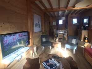 A cozy cabin interior with a TV, wooden furniture, and a dining area.