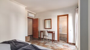 Un dormitorio con cama, escritorio y silla. Se ve un baño por una puerta abierta.