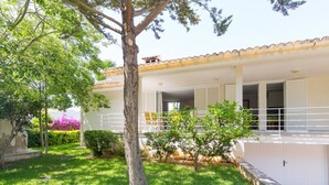 Una casa a due piani con un portico coperto, un piccolo giardino con un albero e vista su una montagna.