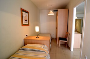 Une petite chambre propre, avec deux lits simples, un bureau, une chaise et un tableau encadré au mur.